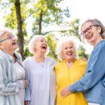 Four older women laughing outdoors in a sunny park