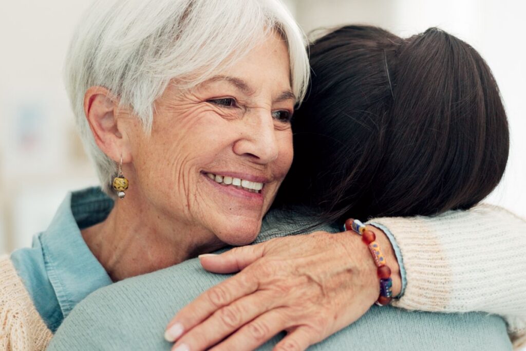 Older woman smiling warmly while receiving a comforting hug, representing emotional support in senior living.