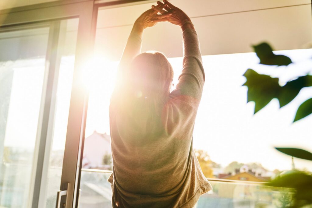 Senior woman stretching toward a sunlit window embracing a fresh start with spring senior living transition tips at Covenant Woods