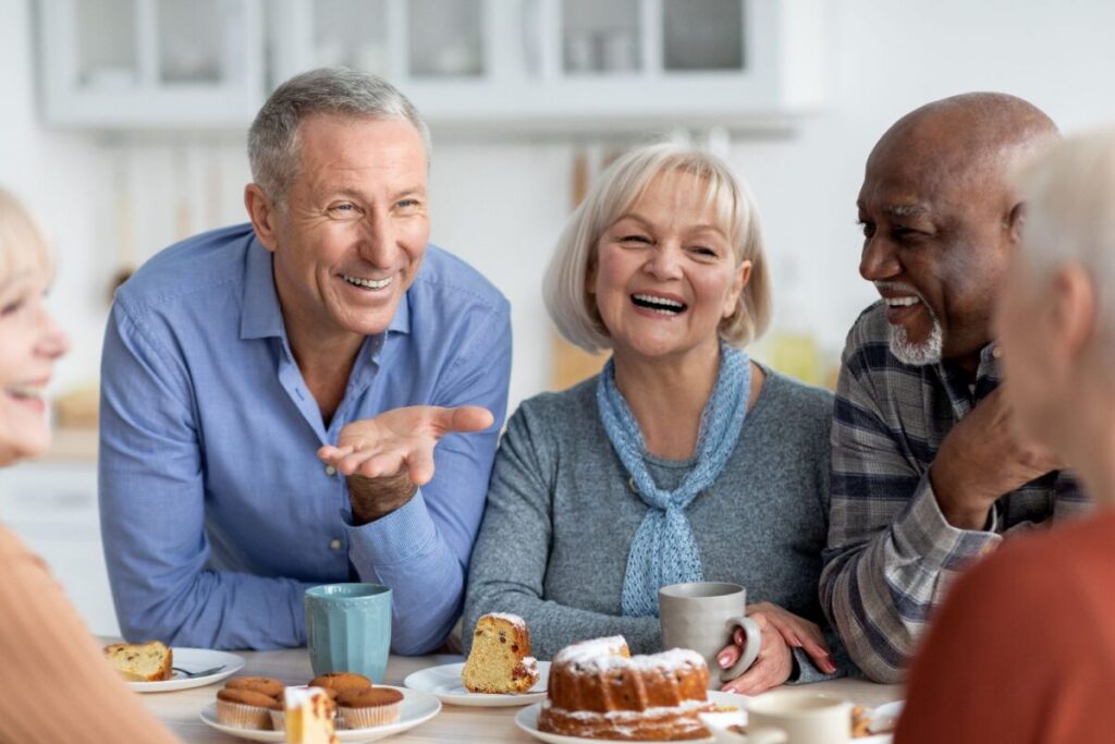 A group of seniors laughing and sharing stories over coffee and pastries, enjoying the kind of everyday social connection for seniors that makes independent living feel like home.