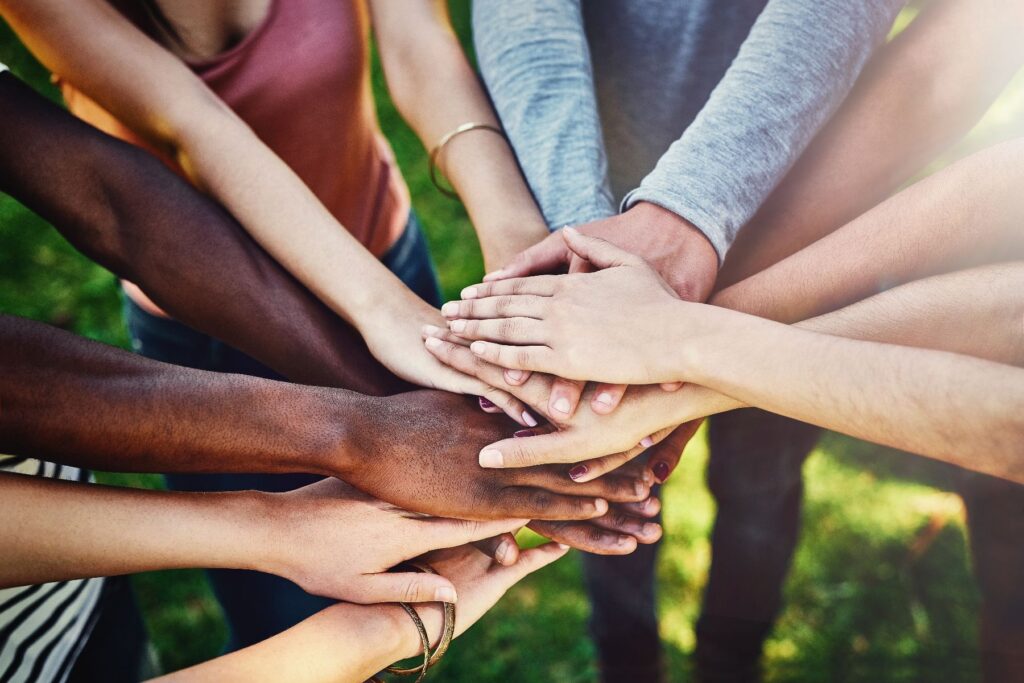 A diverse group of people stack their hands together outdoors, representing the spirit of community building in senior living.